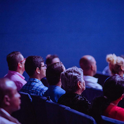 Publikum, welches sich eine Präsentation ansieht, von hinten betrachtet