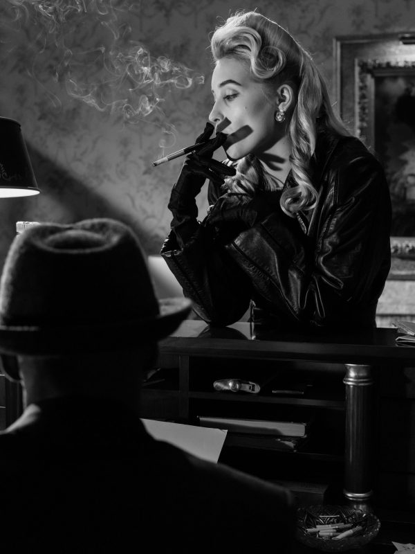 Schwarz-Weiß-Bild einer Blondine im Profil, die an einer Empfangstheke eine Zigarette raucht